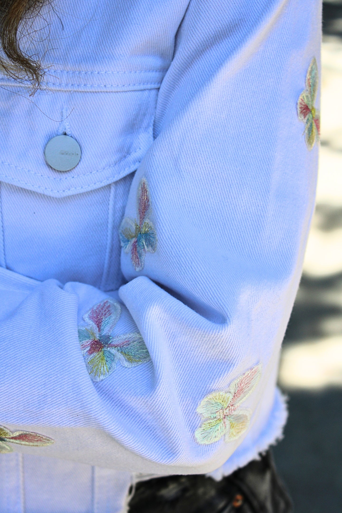 Close-up of rainbow butterfly embroidery on distressed denim sleeve – Veesheh